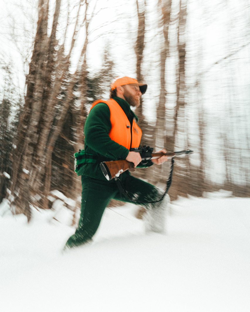 Man wearing solid green Big Woods Bucks brand wool hunting jacket in snowy forest. 