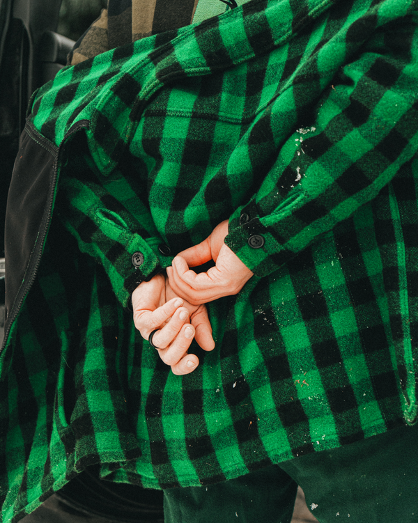 Close-up of hands holding a green and black checkered wool hunting jacket.