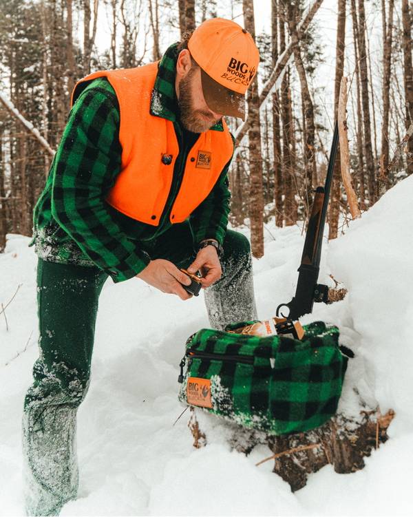 Person in big woods bucks wool hunting gear with a  wool green and black plaid fanny pack in a snowy forest