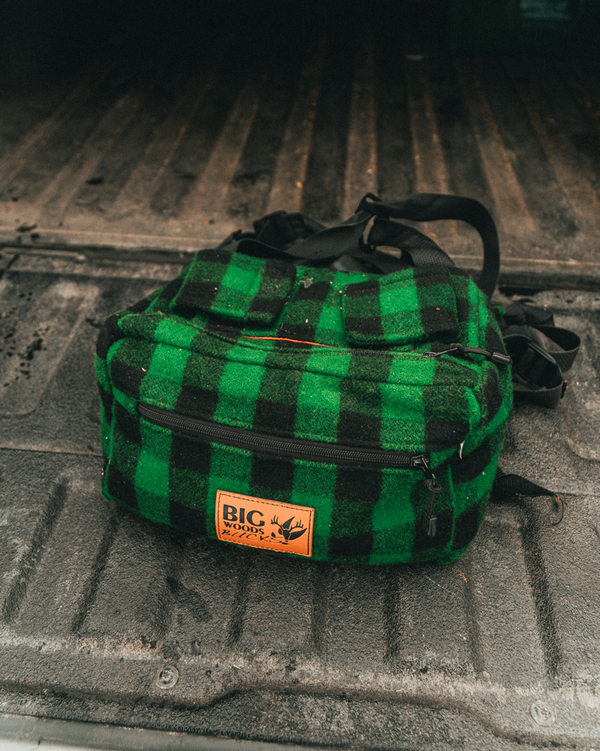 Green and black checkered wool hunting fanny pack with a visible brand logo on a truck tailgate 